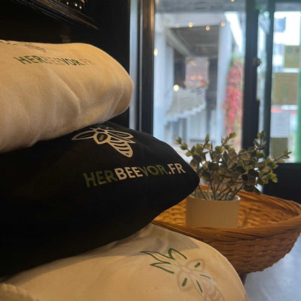 Sweatshirts Herbeevor en coton bio, affichant le logo de la marque spécialisée dans le CBD et le chanvre, présentés en boutique avec un panier en osier et des bières artisanales en arrière-plan.